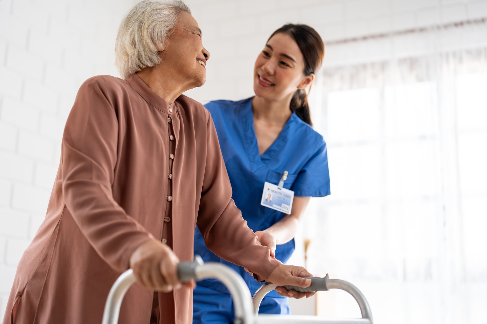 Asian senior older woman patient doing physical therapy with caregiver. Attractive specialist carer women help and support elder mature female practice walking slowly with walker at nursing home care.